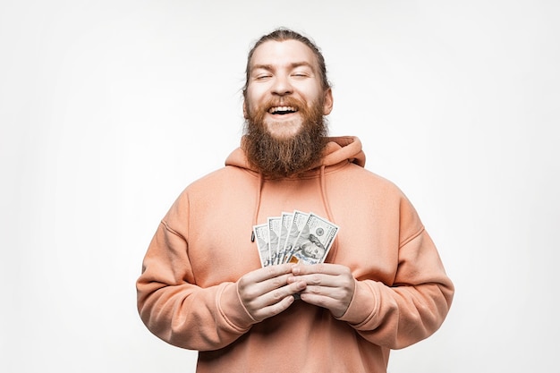 Handsome scandinavian happy man holding dollar currency money in his hands on gray background Guy with ginger hairstyle and beard in a sweatshirt The concept of money salary finance investment