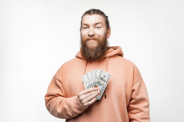 Handsome scandinavian happy man holding dollar currency money in his hands on gray background Guy with ginger hairstyle and beard in a sweatshirt The concept of money salary finance investment