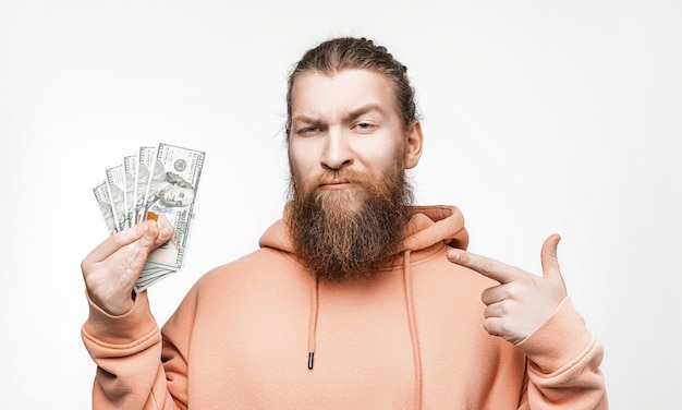 Handsome scandinavian man holding dollar currency money in his hands on gray background Guy with ginger hairstyle and beard in a sweatshirt The concept of money salary finance investment