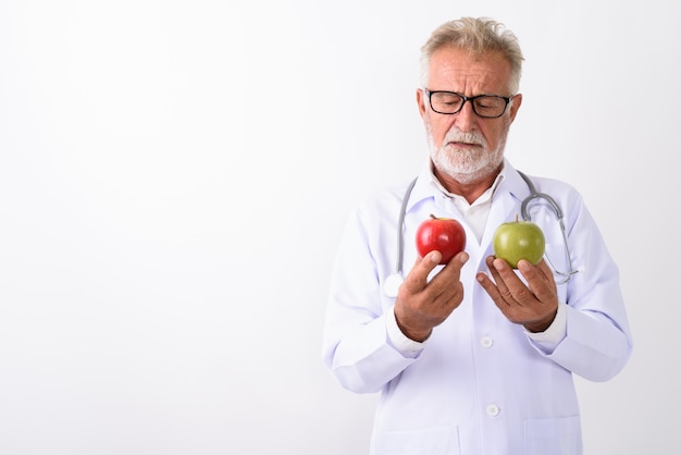 handsome senior bearded man doctor choosing between red apple and green apple on white