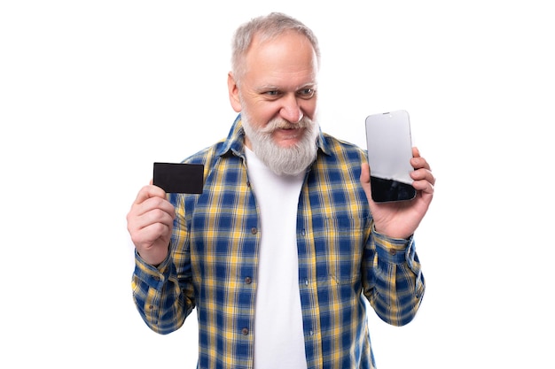 Handsome senior pensioner grayhaired man with a beard in a shirt advertises a card and a smartphone