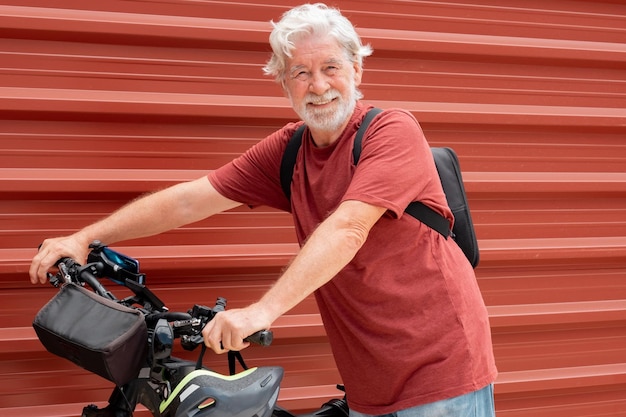 Handsome senior white haired man in urban city with his electric bicycle looking at camera