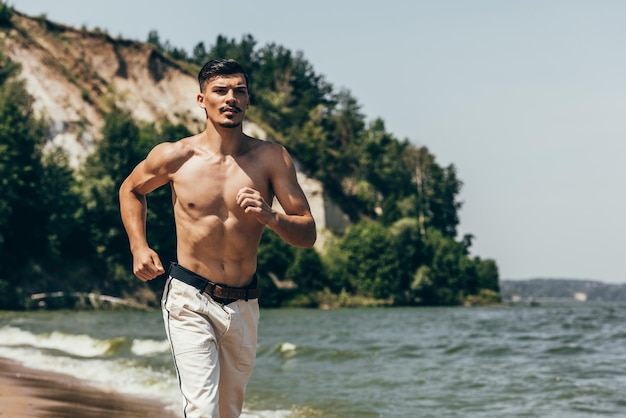 Handsome shirtless man jogging on sandy beach