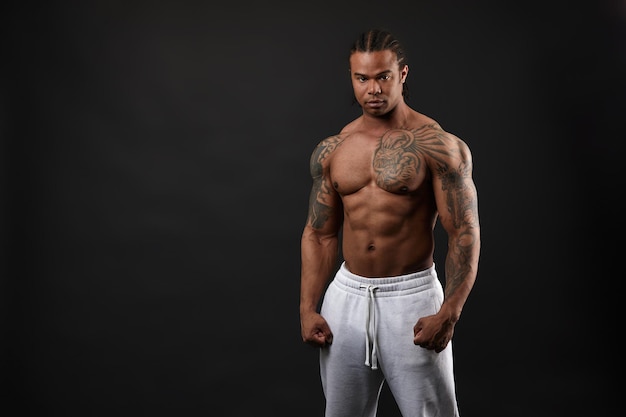 Handsome shirtless muscular black young man looking at camera on dark background in studio shot