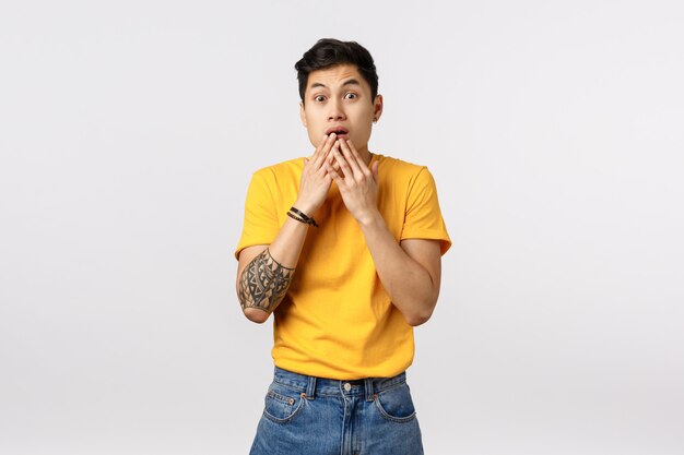 Handsome shocked young asian man in yellow t-shirt