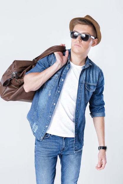 Handsome smiling man in hat and sunglasses carrying leather bag on shoulder