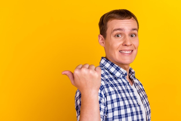 Handsome smiling man pointing away empty space promo isolated on yellow background