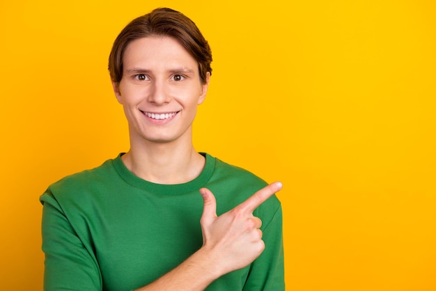 Handsome smiling man pointing away yellow empty space backgroundisolated shopping sale