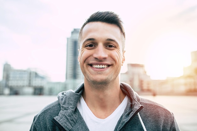 Handsome smiling man in sport wear standing on a cityscape background after jogging