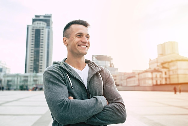 Handsome smiling man in sport wear standing on a cityscape background after jogging