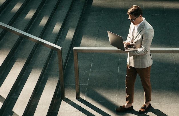 Handsome smiling young business man spending time outdoors at the city using laptop computer on stairs