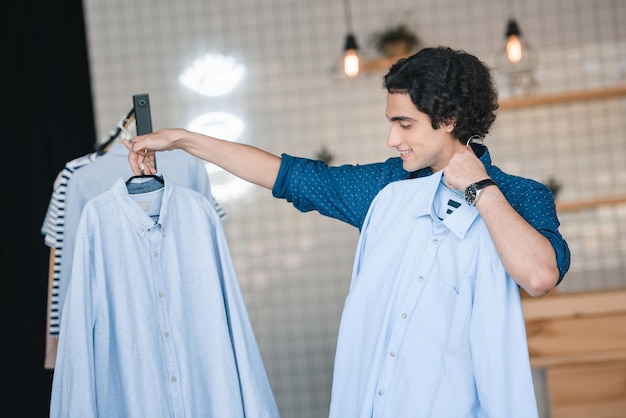 Handsome smiling young man choosing fashionable shirts in boutique