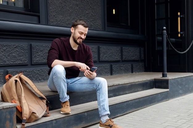 Handsome smiling young man using mobile phone while sitting on steps outdoors