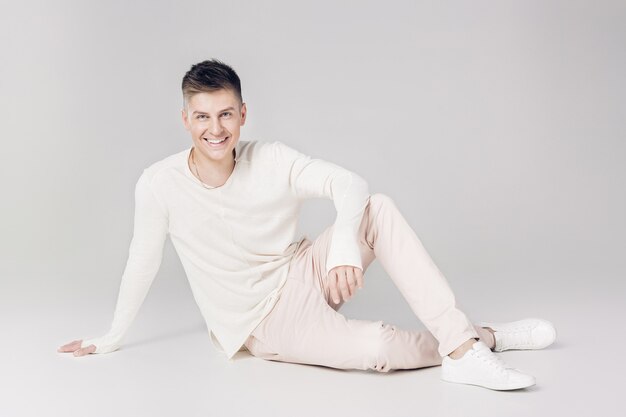 Handsome smiling young man in a white sweater looks at the camera