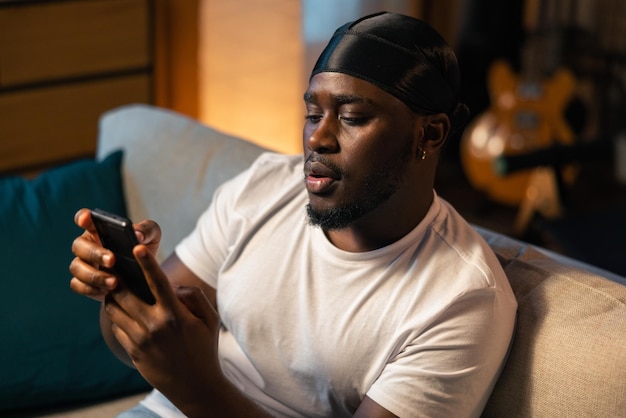 Handsome student relaxing on the sofa reading social media news uploading a new mobile app