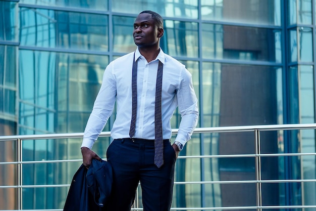 Handsome and stylish African American model groom in a fashionable black jacket and a white shirt with a collar with a elegant tie posing background of Manhattan glass offices cityscape