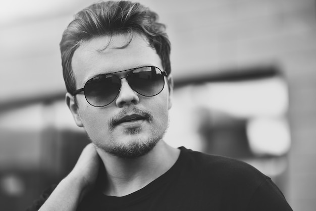 Handsome stylish man with sunglasses and modern hairstyle and beard. Outdoor in the street. black and white photo