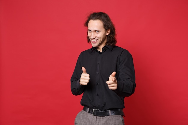 Handsome stylish young curly long haired man in black shirt posing isolated on red wall background studio portrait. People sincere emotions lifestyle concept. Mock up copy space. Looking camera smile.