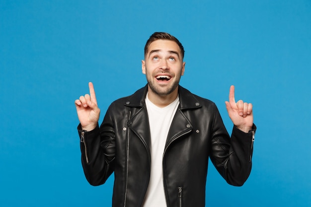 Handsome stylish young unshaven man in black jacket white t-shirt showing on workspace isolated on blue wall background studio portrait. People sincere emotions lifestyle concept. Mock up copy space.