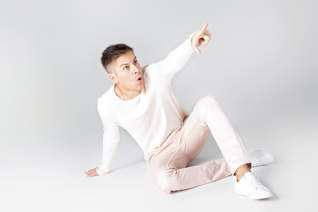 Handsome surprised man in a white sweater pointing in one direction