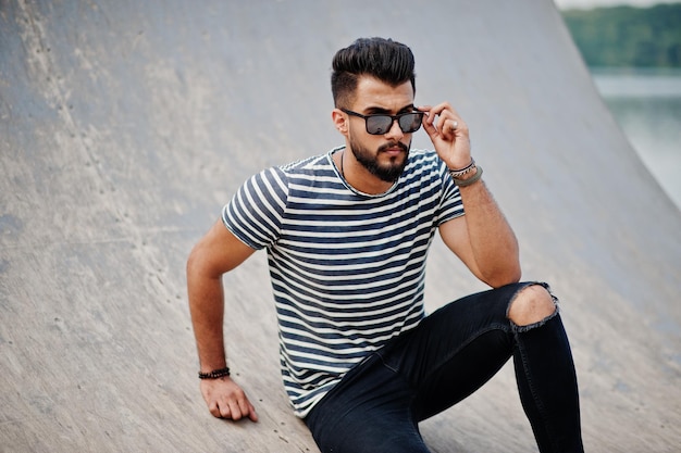 Handsome tall arabian beard man model at stripped shirt posed outdoor Fashionable arab guy at sunglasses