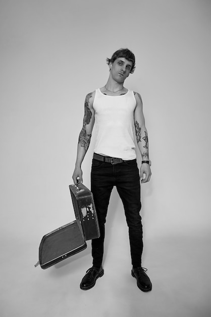 Handsome tattooed young man in white tshirt standing against light background in studio shot