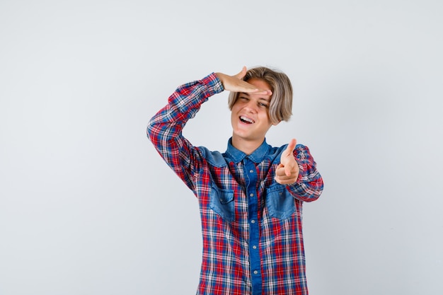 Handsome teen boy in checked shirt pointing forward, with hand over head and looking energetic , front view.