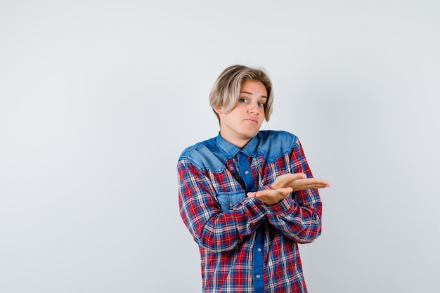 Handsome teen boy in checked shirt showing helpless gesture and looking hesitative , front view.