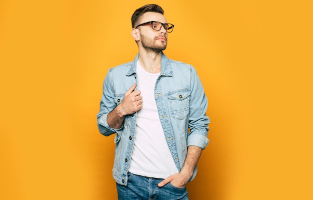 Handsome trendy and stylish beard man in denim shirt is posing over yellow background