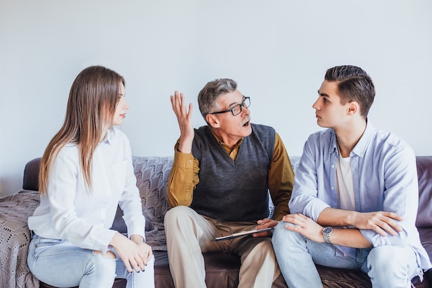 Handsome unhappy man sitting with his wife on the sofa on therapy with psychologist