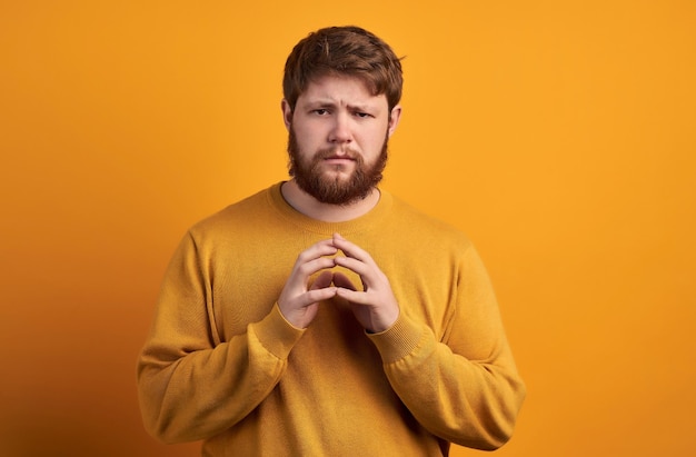 Handsome unshaven man has tricky evil plan steepls fingers and looks mysteriously at camera thinks over good idea wears casual sweater and spectacles poses over rosy background copy space