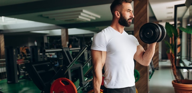 Handsome weightlifter lifting bench press working out with dumbbell in the gym