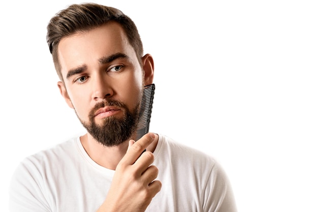 Handsome well groomed man combing his beard on white background