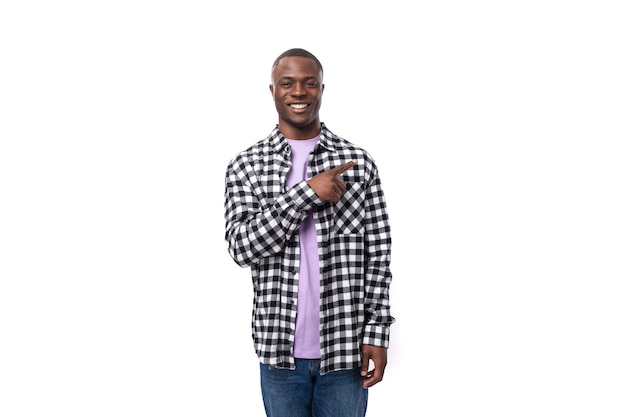 Handsome year old african guy dressed in a plaid black and white shirt points with his hand on the