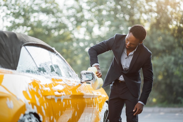 Handsome young African American businessman cleaning rearview car mirror