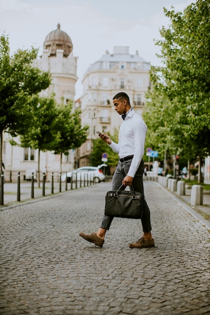 Handsome young African American businessman using a mobile phone while ceossing a street