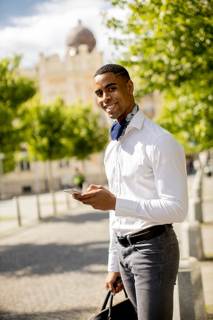 Handsome young African American businessman using a mobile phone while waitng for a taxi on a street