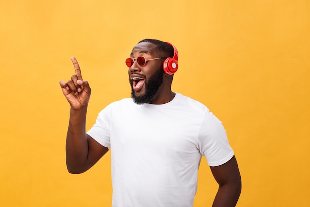 Handsome young African American man listening and smiling with music on his mobile device Isolated over yellow background