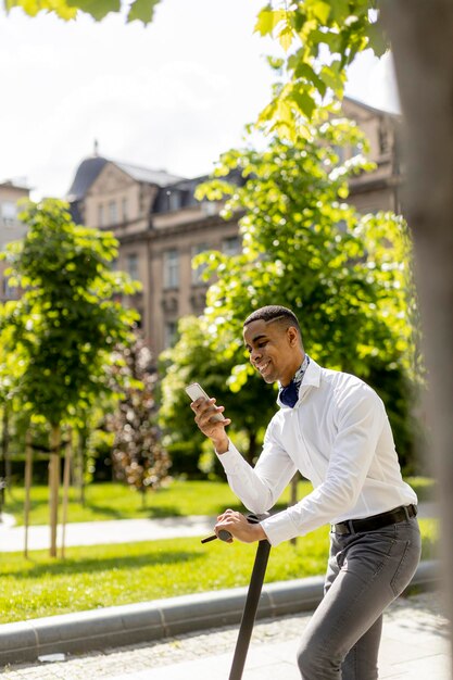 Handsome young African American using mobile phone while standing with electric scooter on a street