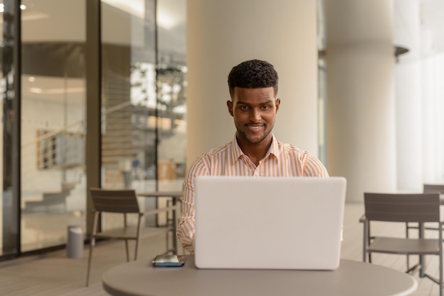 Handsome young African businessman working in city using laptop computer at coffee shop