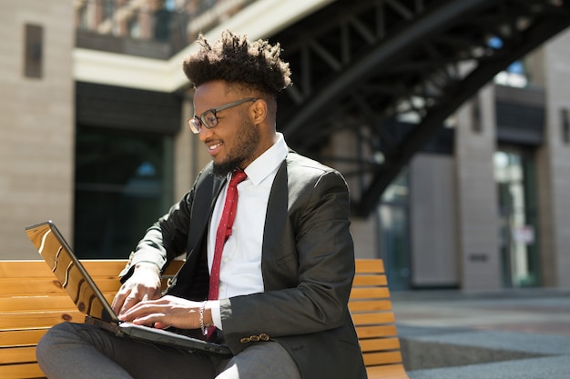 handsome young african man on bench with laptop in summer