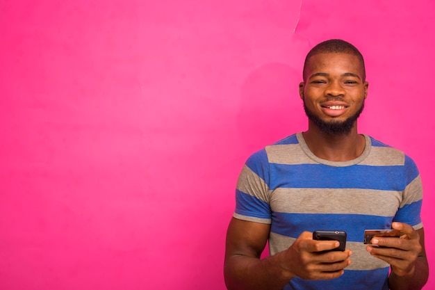 handsome young african man isolated over pink background holding his credit card and smart phone