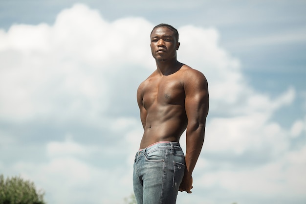 handsome young african man with muscles against the sky