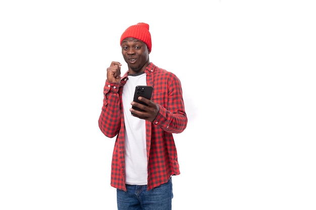 Handsome young american man in red headwear sitting on internet using smart phone on isolated white