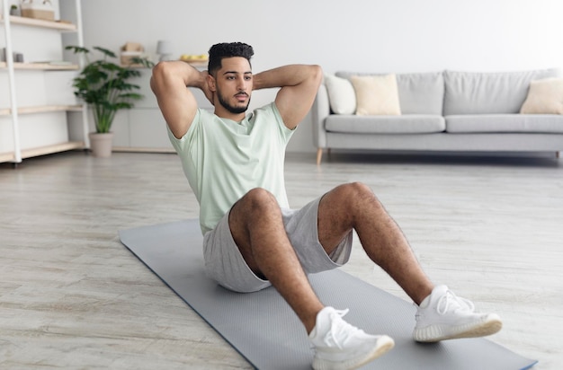 Handsome young arab man exercising on yoga mat strengthening abs muscles at home copy space