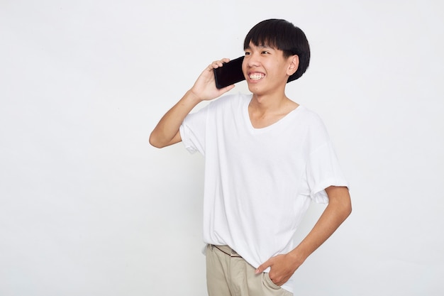 Handsome young Asian man showing a phone to empty space isolated white surface