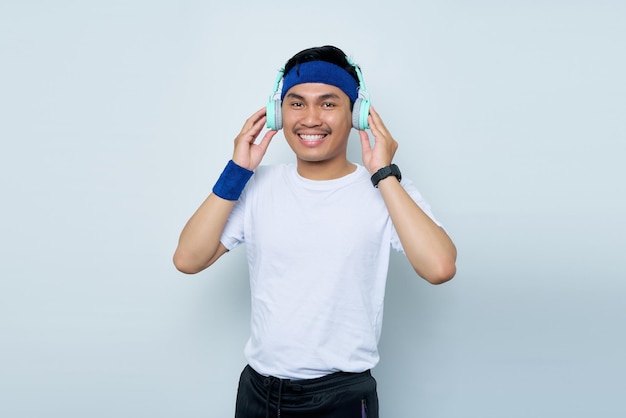 Handsome young asian man sporty fitness trainer instructor in blue headband and white tshirt Makes fun Listening to music with headphones isolated over white background