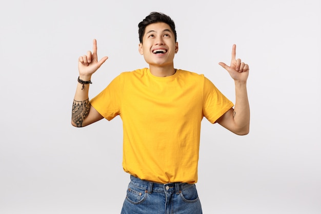 Handsome young asian man in yellow t-shirt pointing up