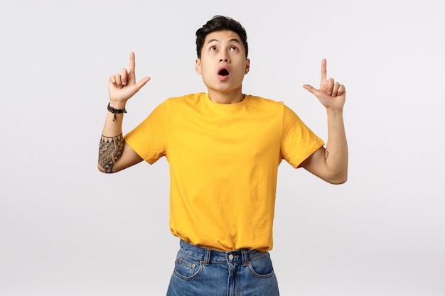 Handsome young asian man in yellow t-shirt pointing up