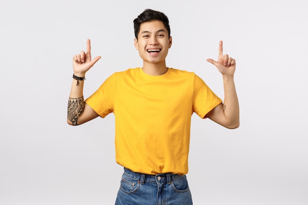 Handsome young asian man in yellow t-shirt pointing up